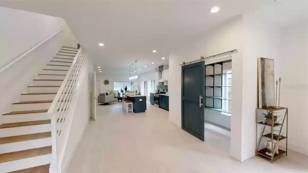 Interior hallway with staircase, sliding barn-style pantry door, and open kitchen beyond